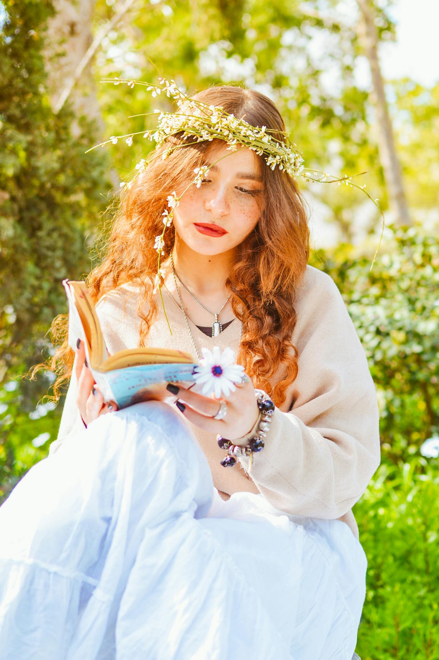 Young woman with floral crown reading a book in sunny garden setting.